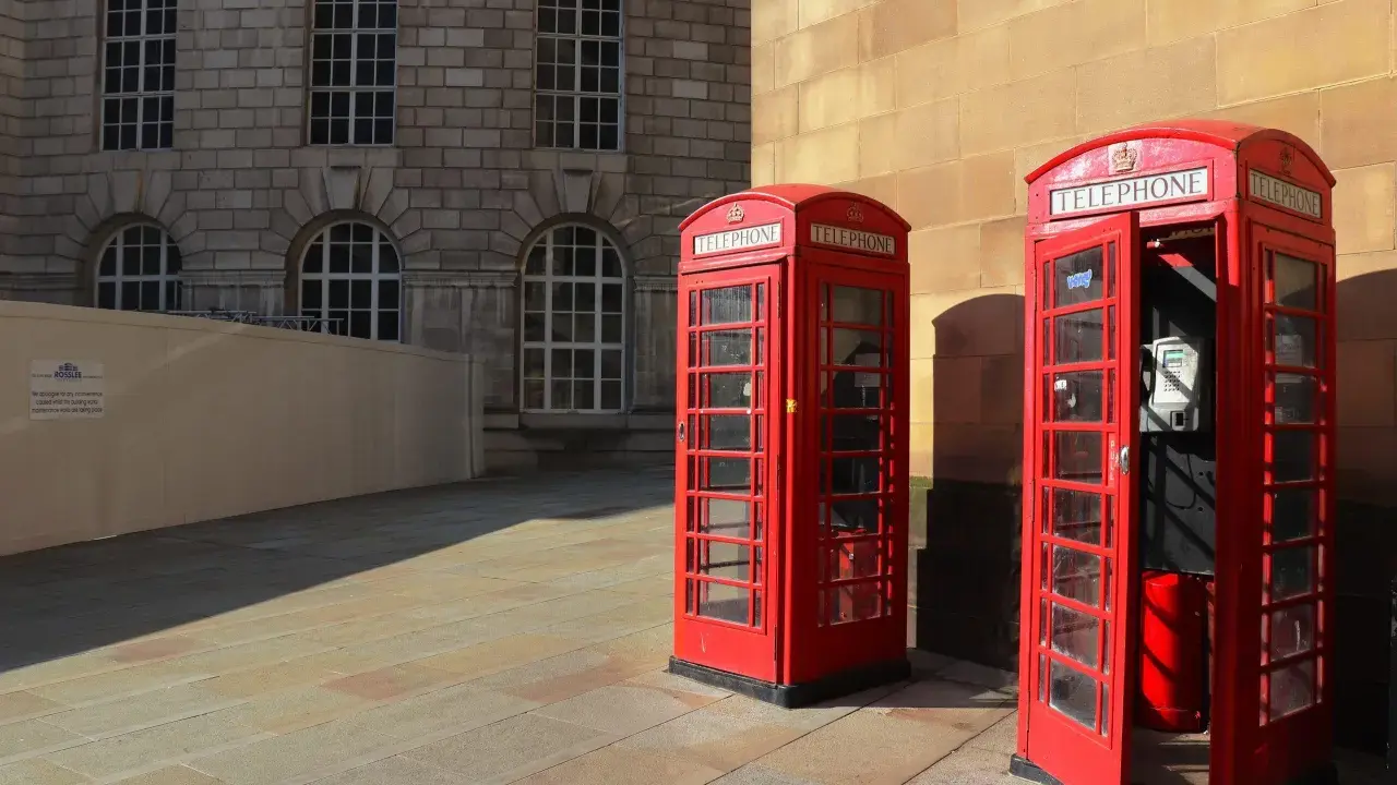 Klasyczne czerwone budki telefoniczne na brukowanym placu, w tle kamienna fasada budynku. Manchester miasto.