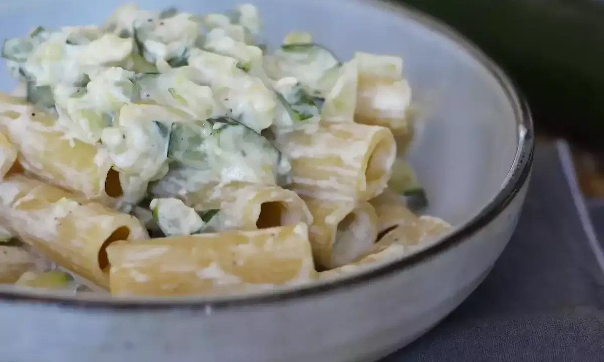 En krämig zucchini pasta i en skål, med en hel zucchini i bakgrunden.