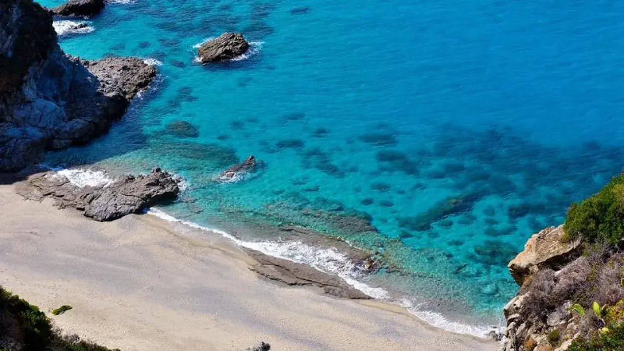 Spiaggia dorata e mare cristallino con scogli a Capo Cozzo.