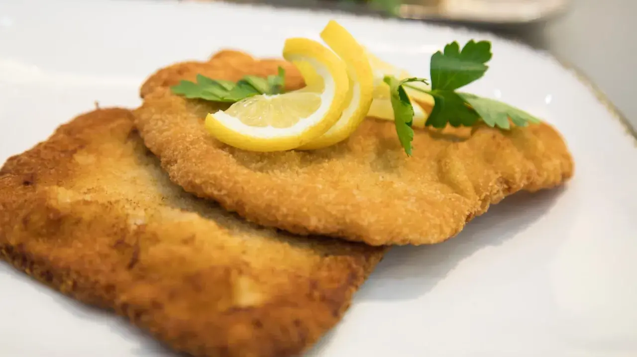 Zwei goldbraune Schnitzel, perfekt in Butter gebraten, garniert mit Zitronenspalten und Petersilie auf einem weißen Teller.