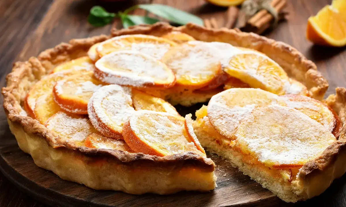 Une délicieuse tarte à l'orange, garnie de fines tranches d'agrumes et saupoudrée de sucre glace, sur un fond de bois rustique.