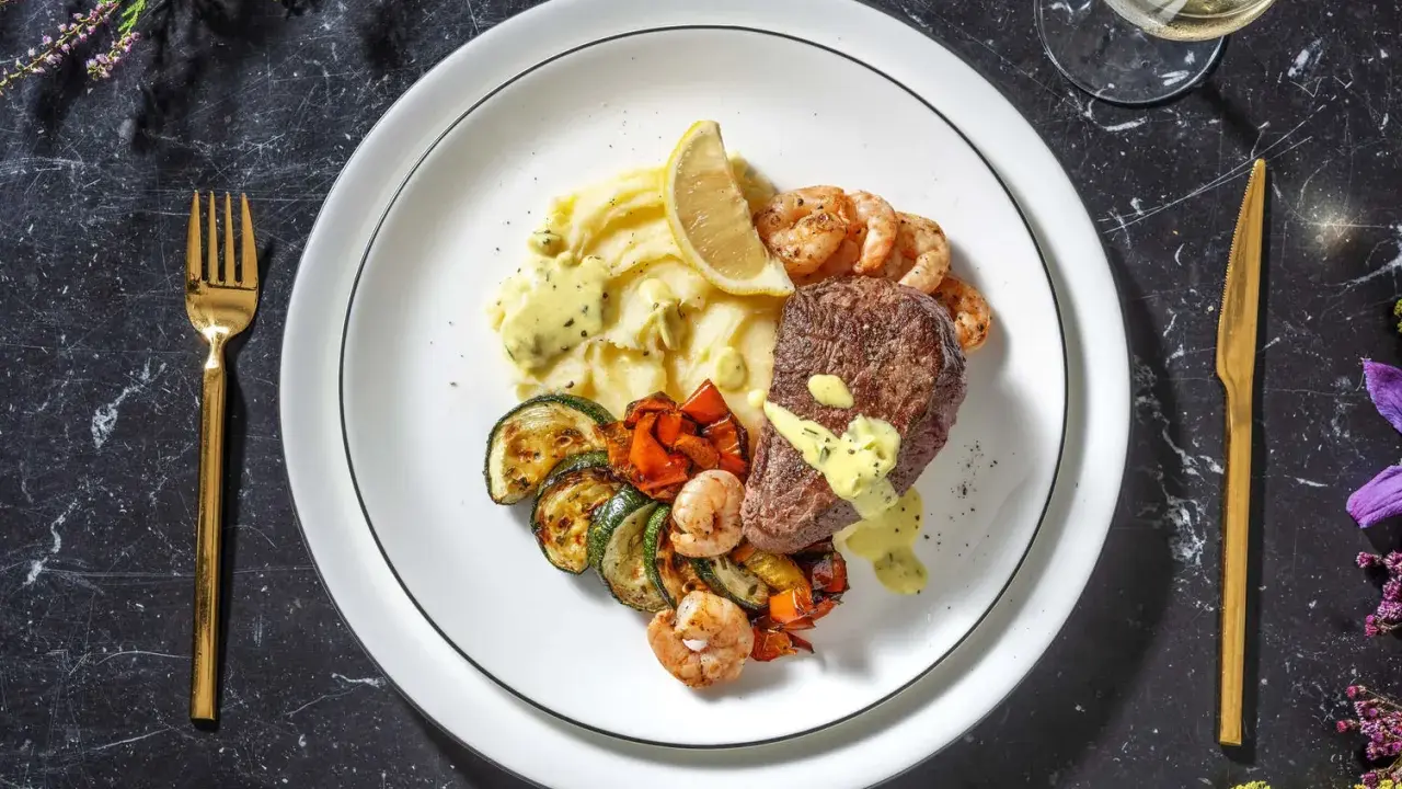 Ein köstliches Surf and Turf Rezept: saftiges Steak, Garnelen, Kartoffelpüree und gegrilltes Gemüse auf einem Teller.