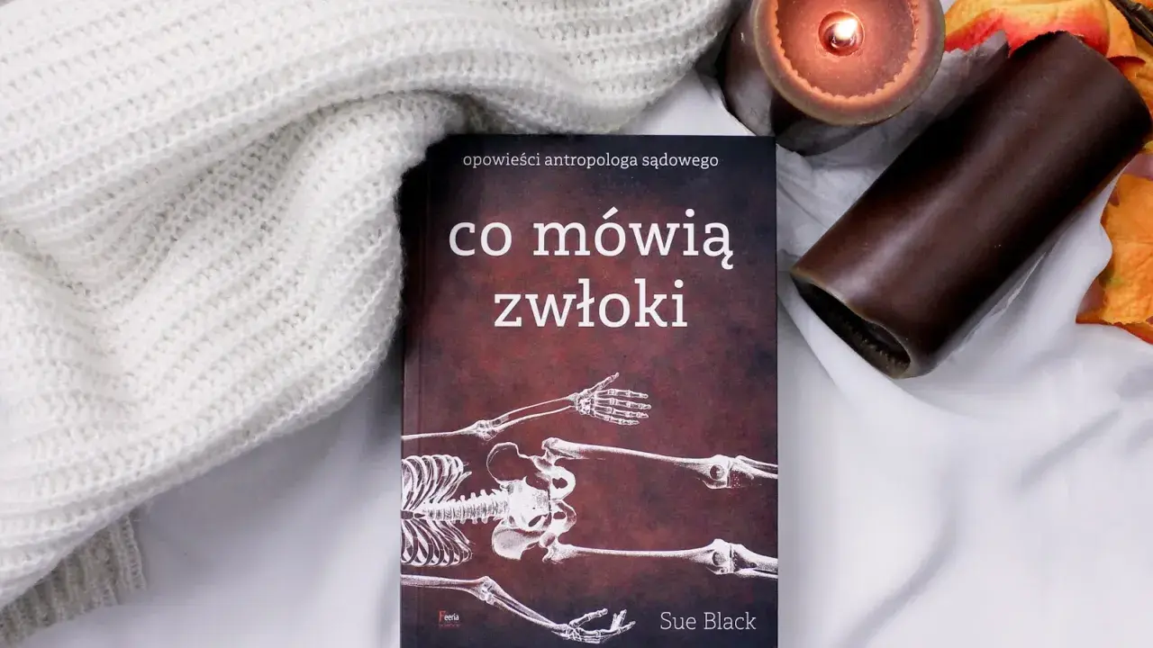 Książka "Co mówią zwłoki" Sue Black, opowieści antropologa sądowego, leży obok zapalonej świecy i jesiennych liści.