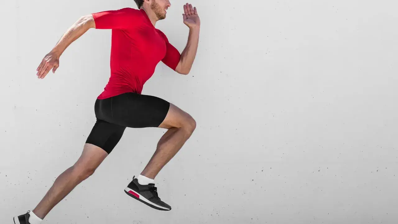 Ein Mann in rotem Shirt und schwarzen Shorts läuft mit hoher Kadenz gegen eine Betonwand.