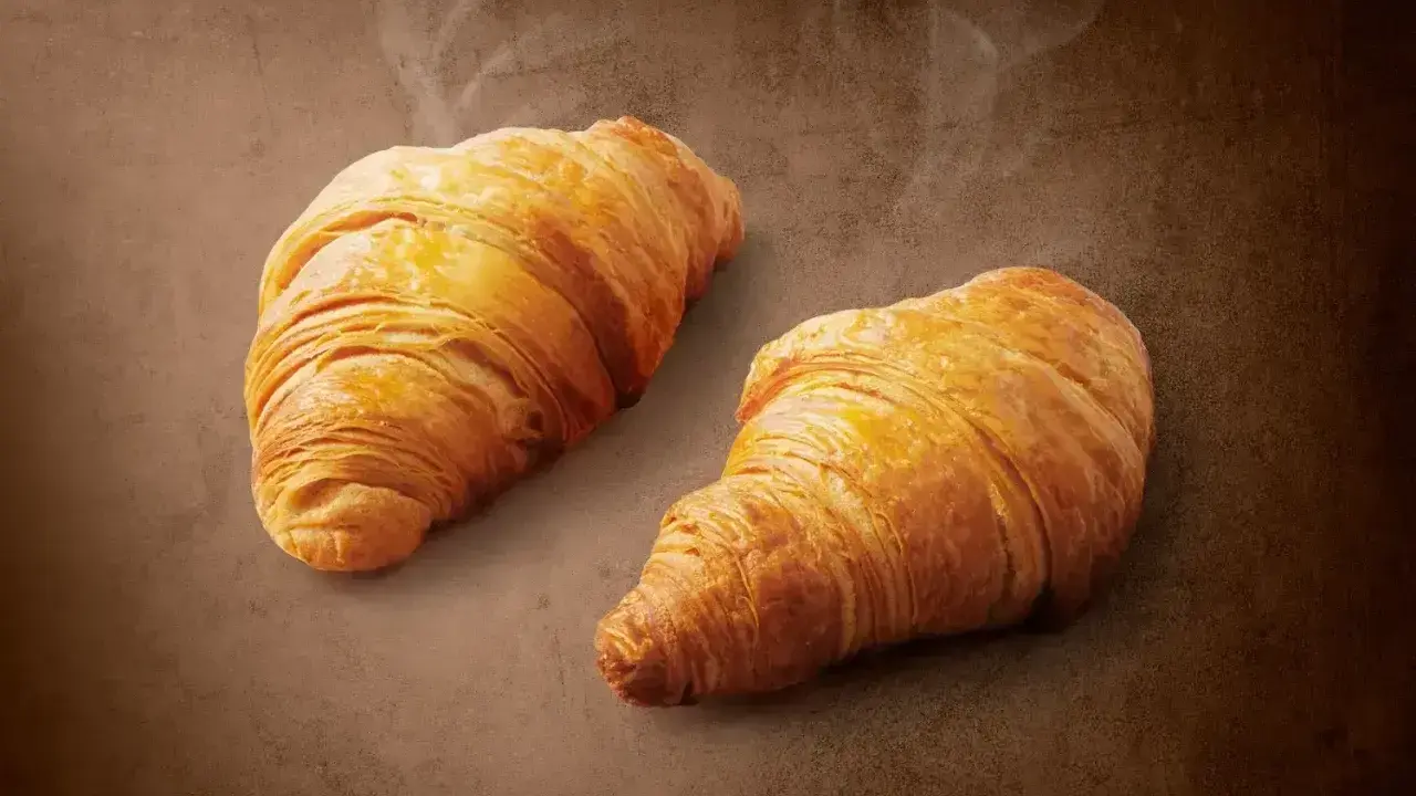 Dwa złociste, parujące croissanty na brązowym tle. Pyszne, choć warto pamiętać o ich kaloryczności.