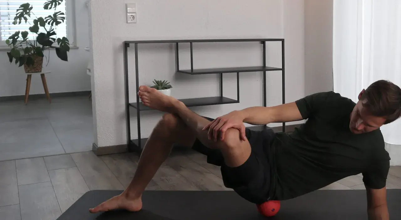 Mann dehnt den Piriformis mit einem roten Ball unter der Hüfte.