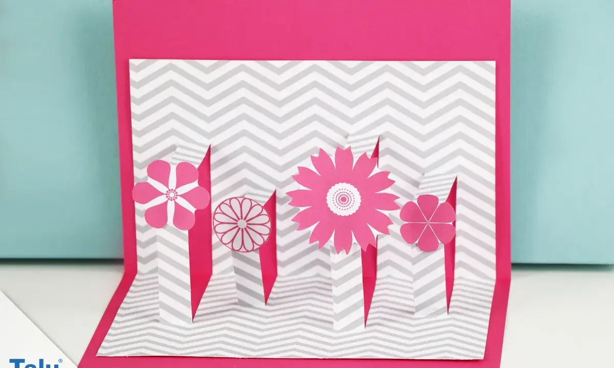 Eine pinke Pop-up-Karte basteln mit Blumen auf grau-weißem Zickzack-Muster.