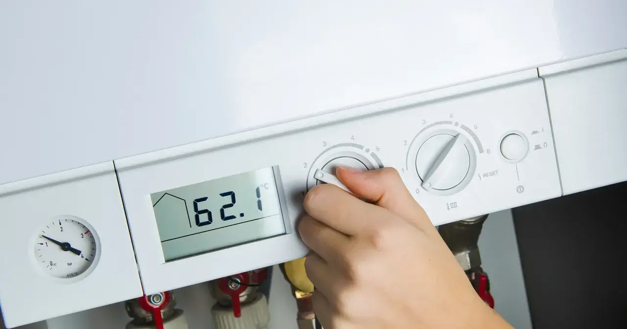 Dłoń reguluje ustawienie pieca gazowego. Na wyświetlaczu 62.1°C, obok manometr i pokrętła regulacji.
