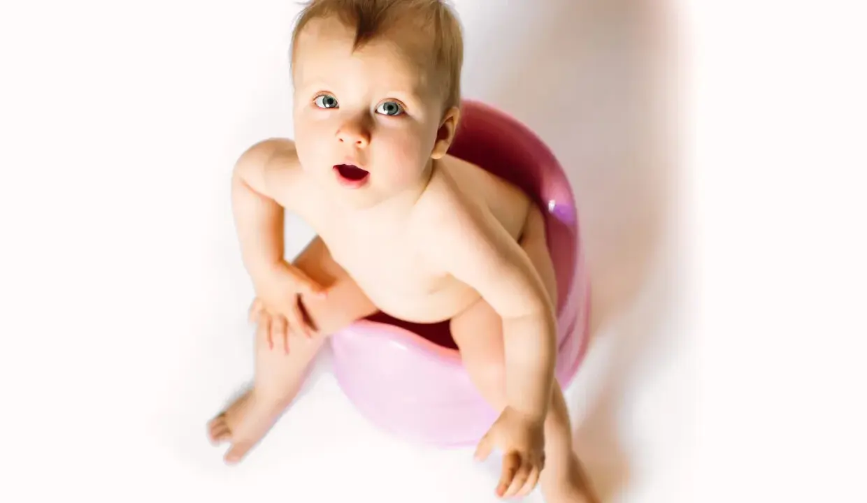 Bambino seduto sul vasino rosa, con espressione sorpresa. Attenzione alla cistite nei bambini.