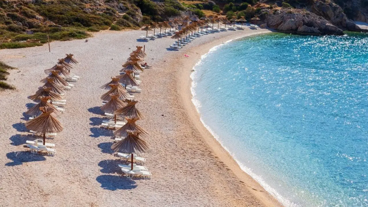 Rządki parasoli i leżaków na kamienistej plaży, obok krystalicznie czystej, turkusowej wody. To jedna z najpiękniejszych plaż w Europie, idealna na relaks.