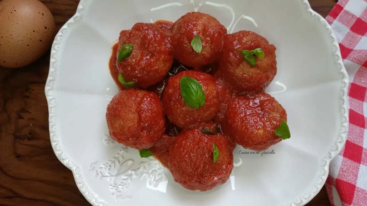 Pallotte cacio e ova in salsa di pomodoro, guarnite con basilico fresco. Un uovo intero è visibile a sinistra.