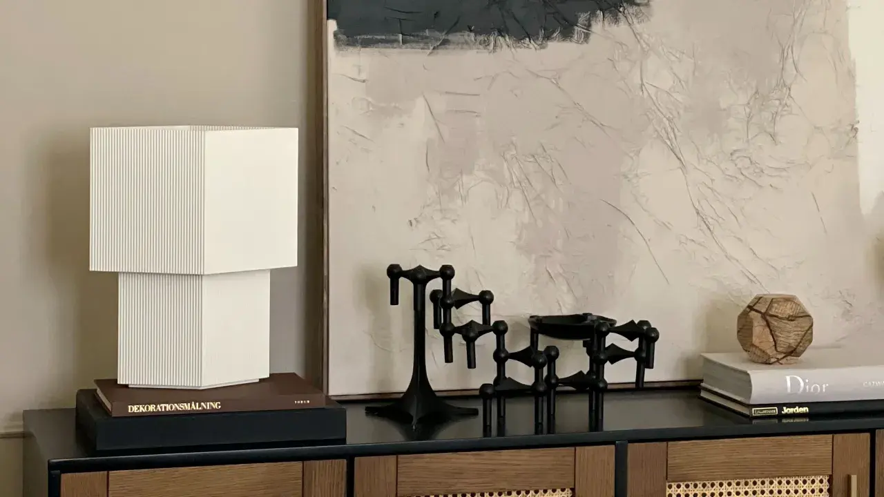 En stilren stilleben inredning med en vit lampa, svarta ljusstakar och en bok med texten "Dior".