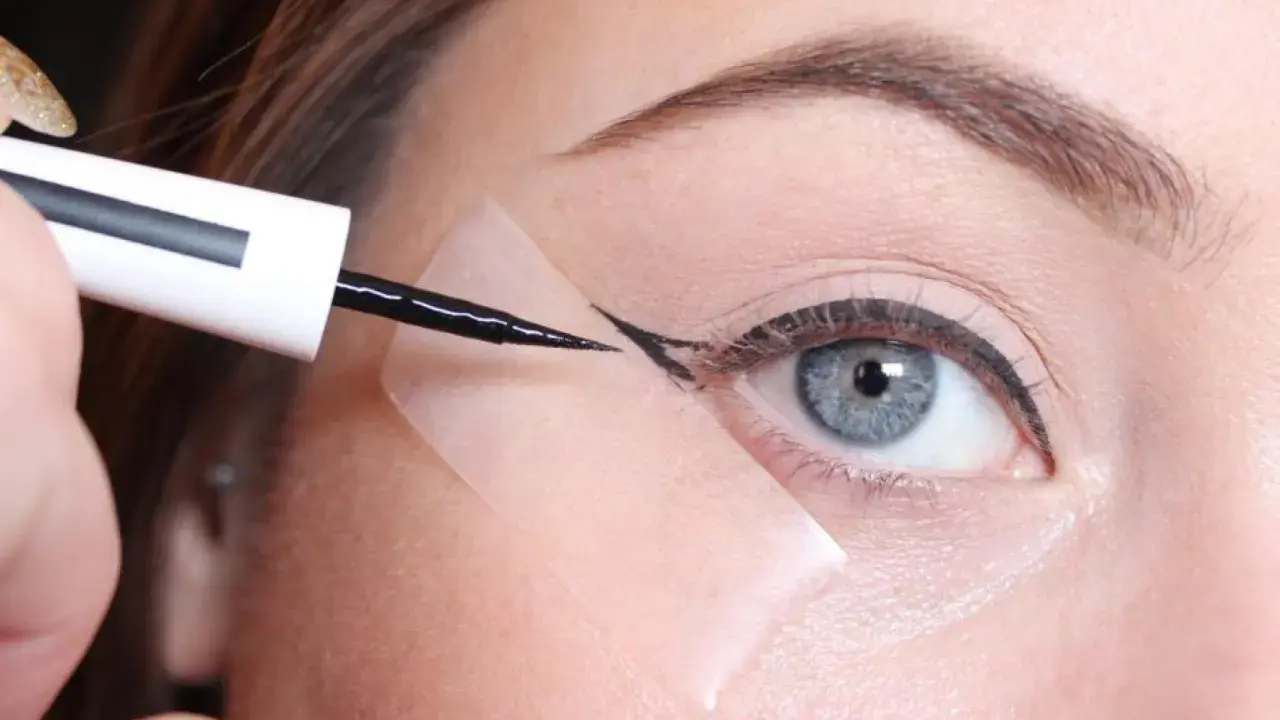 Aplicando delineador con cinta para aprender como hacer la raya del ojo para principiantes. Ojo azul, ceja definida, delineador negro.