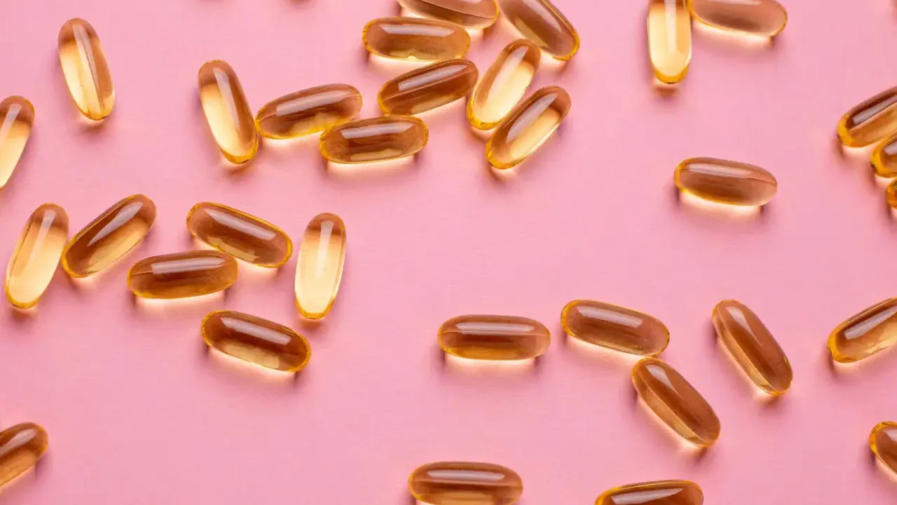 Capsule dorate sparse su sfondo rosa, utili per la vitamina D in gravidanza.