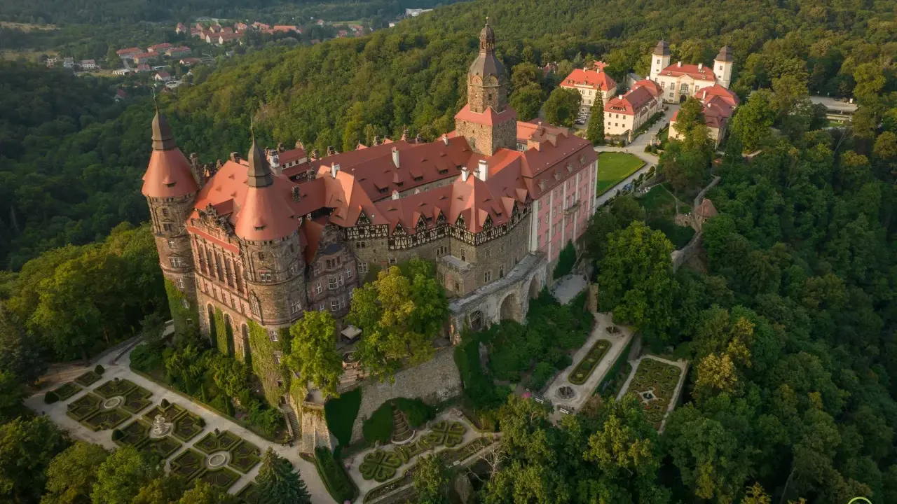 Zamek Książ w górach wałbrzyskich, otoczony bujną zielenią, z malowniczymi ogrodami i wieżami.