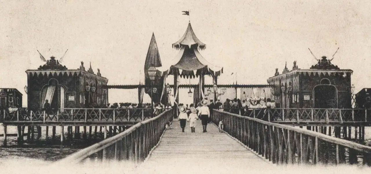 Antica passeggiata sui bagni isola di Cervia, con bambini che camminano sul pontile verso le strutture sul mare.