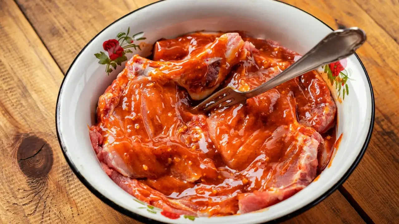 Morceaux de viande crue dans une sauce rouge épicée, prêts à être cuisinés. Une fourchette est plantée dans la préparation.