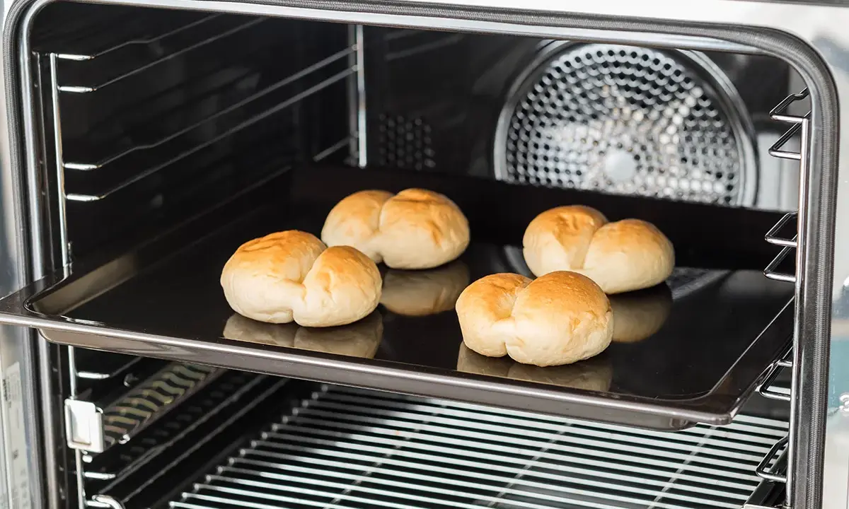Cinq petits pains dorés sur une plaque de cuisson dans un four. C'est une bonne question : qu'est-ce qu'un lèchefrite ? C'est cette plaque !
