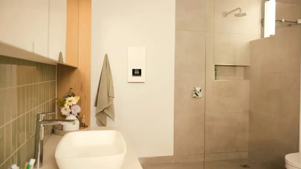 Modernes Bad mit Dusche und Waschbecken. Ein Durchlauferhitzer hängt an der Wand, der für warmes Wasser sorgt, auch wenn man ihn an 230V anschließen möchte.