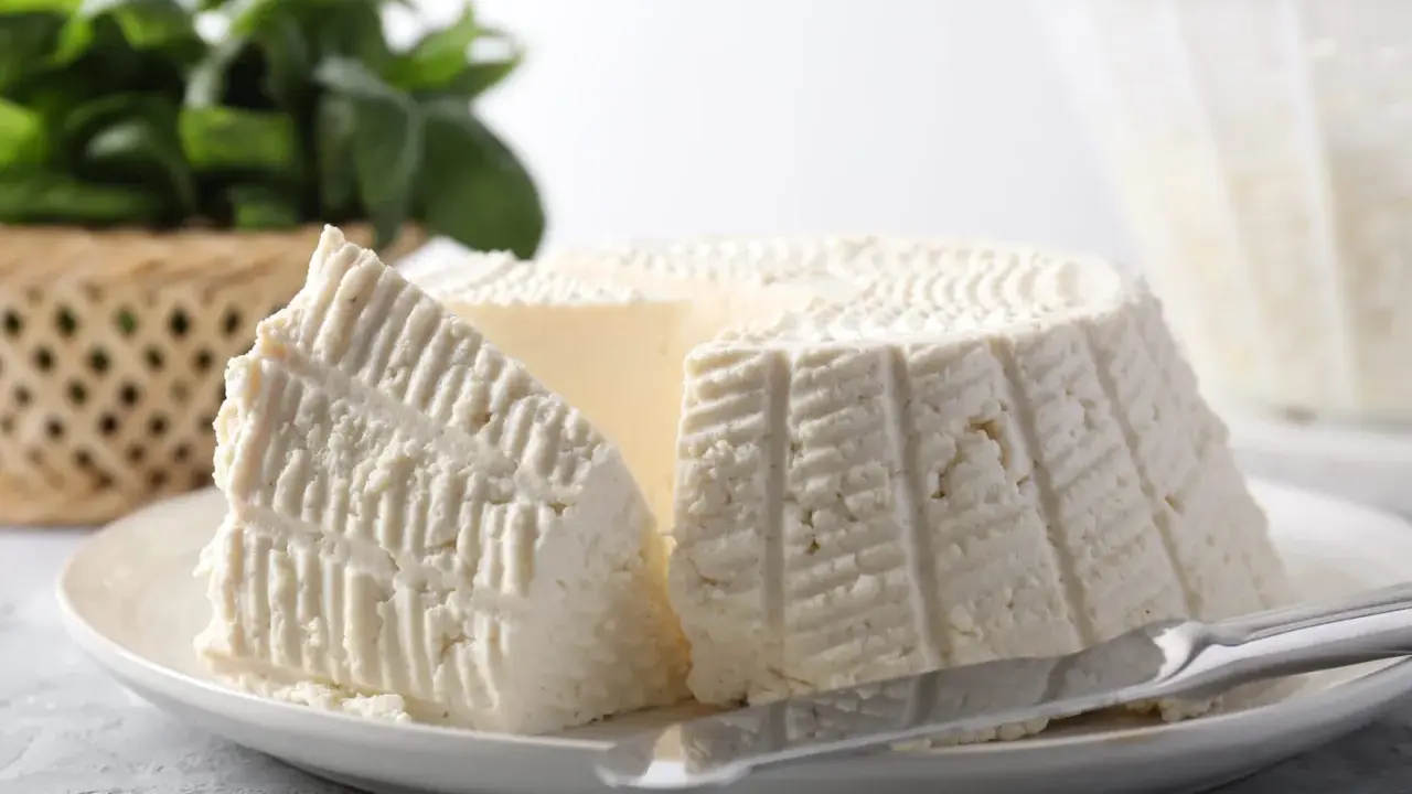 Un morceau de ricotta fraîche sur une assiette, avec des herbes en arrière-plan. Idéal pour connaître les calories de la ricotta.