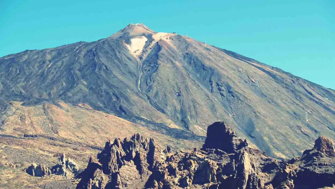 Vulkan Pico del Teide mit felsiger Landschaft im Vordergrund und blauem Himmel.