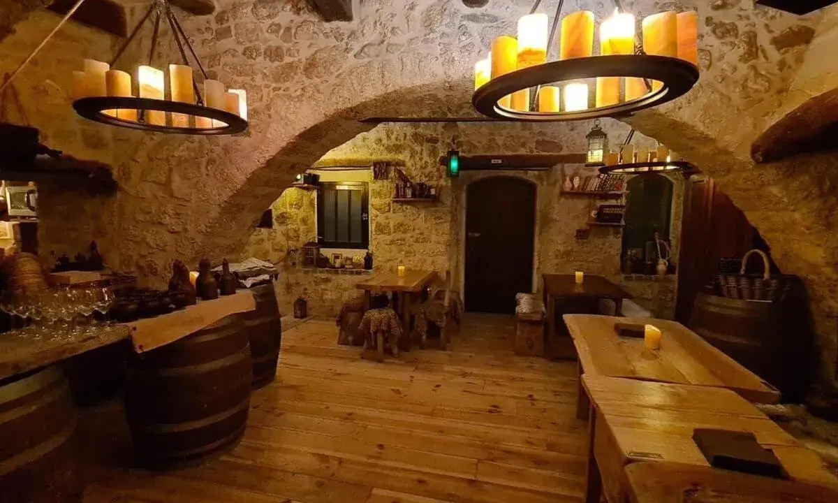 Intérieur d'une taverne médiévale avec murs en pierre, tables en bois et chandeliers. Le tavernier moyen âge y servirait sûrement de l'hydromel.