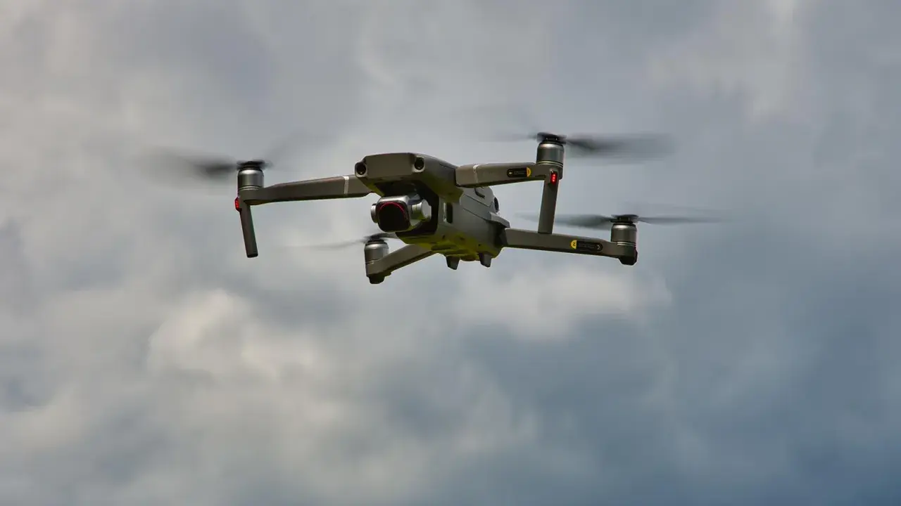 Eine graue Drohne mit roten Lichtern fliegt im bewölkten Himmel. Man kann die Propeller sehen, die sich drehen, während die Drohne in der Luft schwebt. Es ist ein tolles Gefühl, eine Drohne fliegen zu lassen.