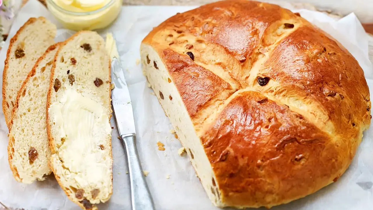 Ein goldbraunes Osterbrot mit Rosinen, aufgeschnitten und mit Butter bestrichen. Perfekt für ein Osterbrot Rezept.