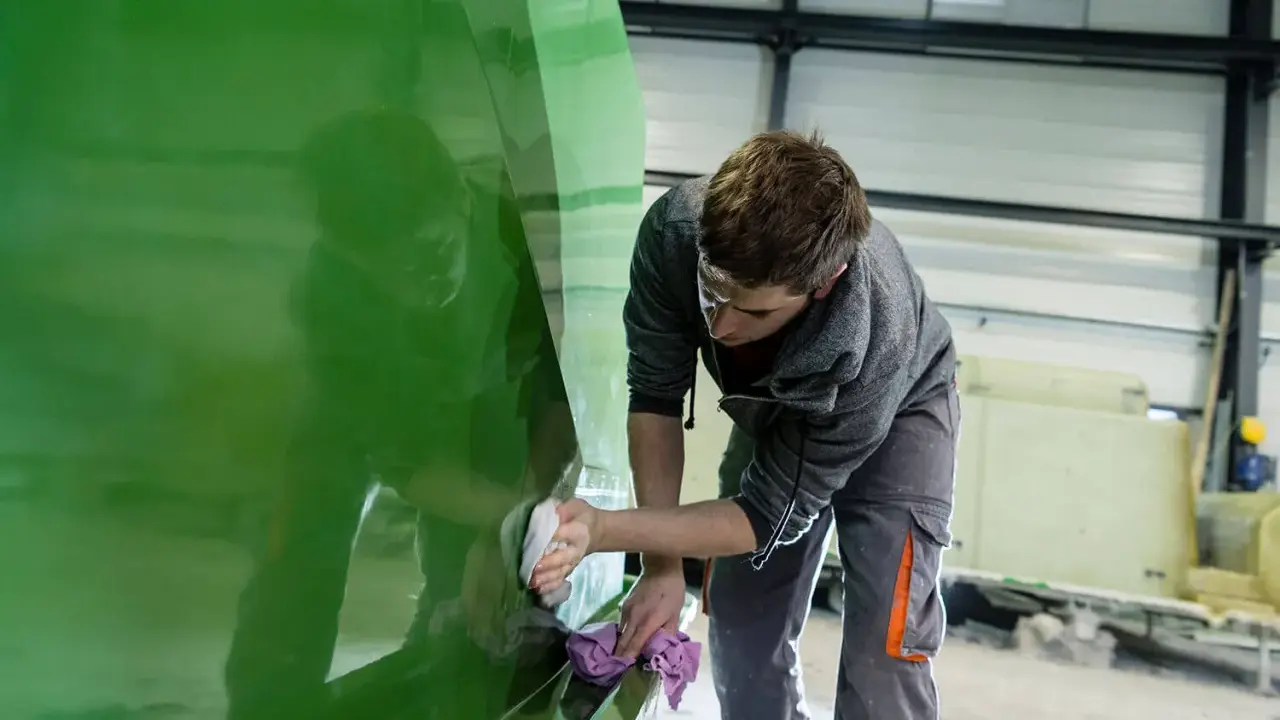 Un ouvrier polit la coque d'un bateau en polyester vert vif dans un atelier.