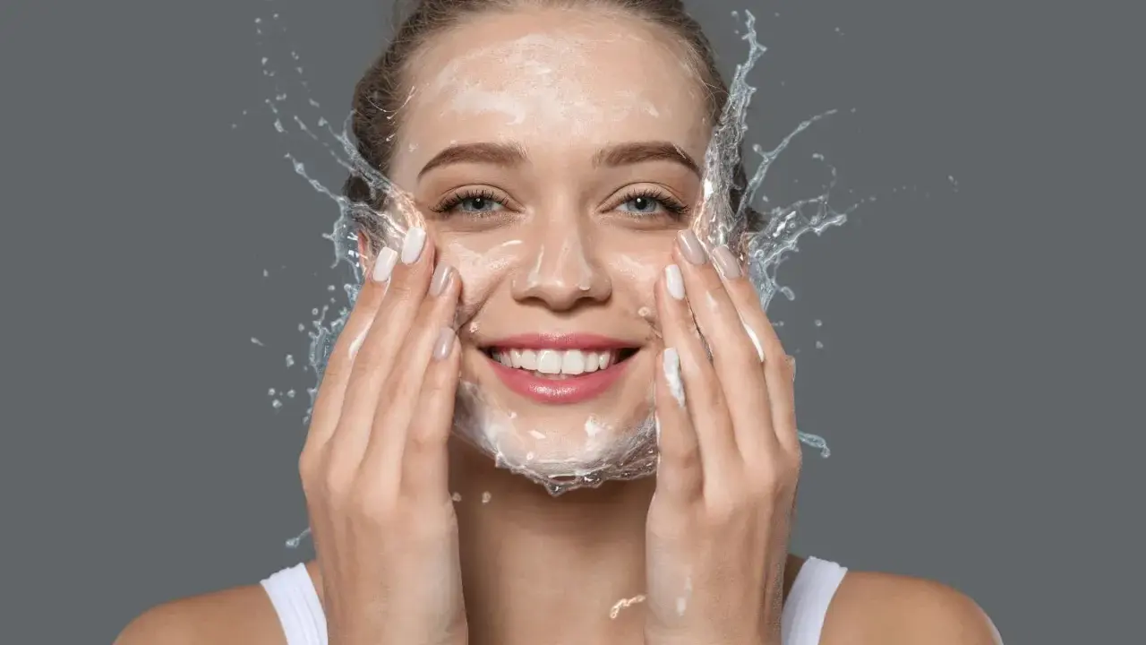 Mujer sonriente con espuma y agua en la cara, disfrutando de su rutina de doble limpieza.