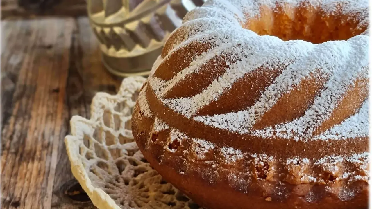 Ciambellone allo yogurt soffice e profumato, cosparso di zucchero a velo su un centrino di pizzo, pronto per essere gustato.
