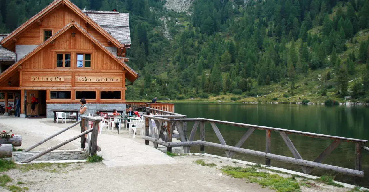 Rifugio sul lago nambino, con tavoli all'aperto e un bosco di conifere sullo sfondo.