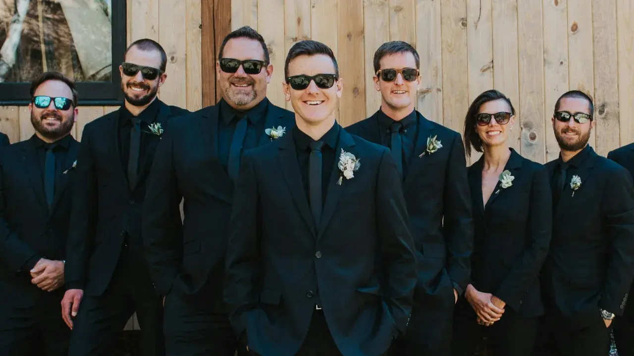Groomsmen in matching black suits and sunglasses, showcasing stylish black suit ideas for a wedding party.