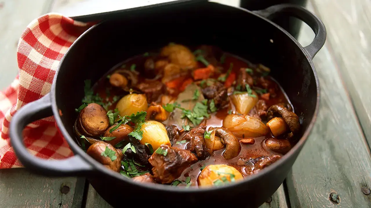 En mustig boeuf bourguignon i gjutjärnsgryta med champinjoner, lök och örter.