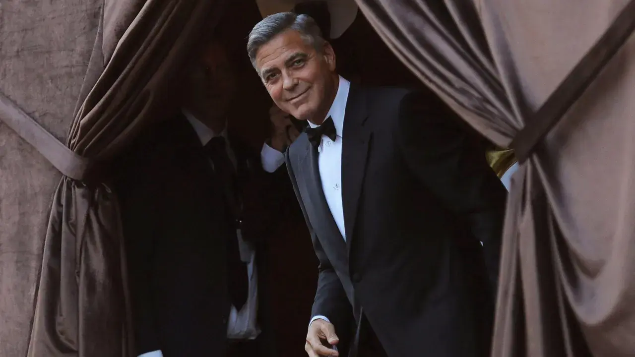 George Clooney, dapper in a tuxedo, emerges from behind velvet curtains. A perfect tix vs suit moment.