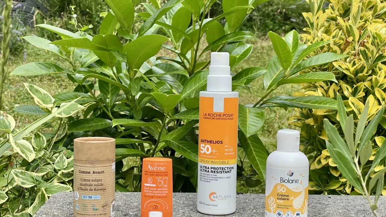 Quatre produits de protection solaire, dont un écran solaire physique, sont alignés sur un muret, entourés de verdure luxuriante.