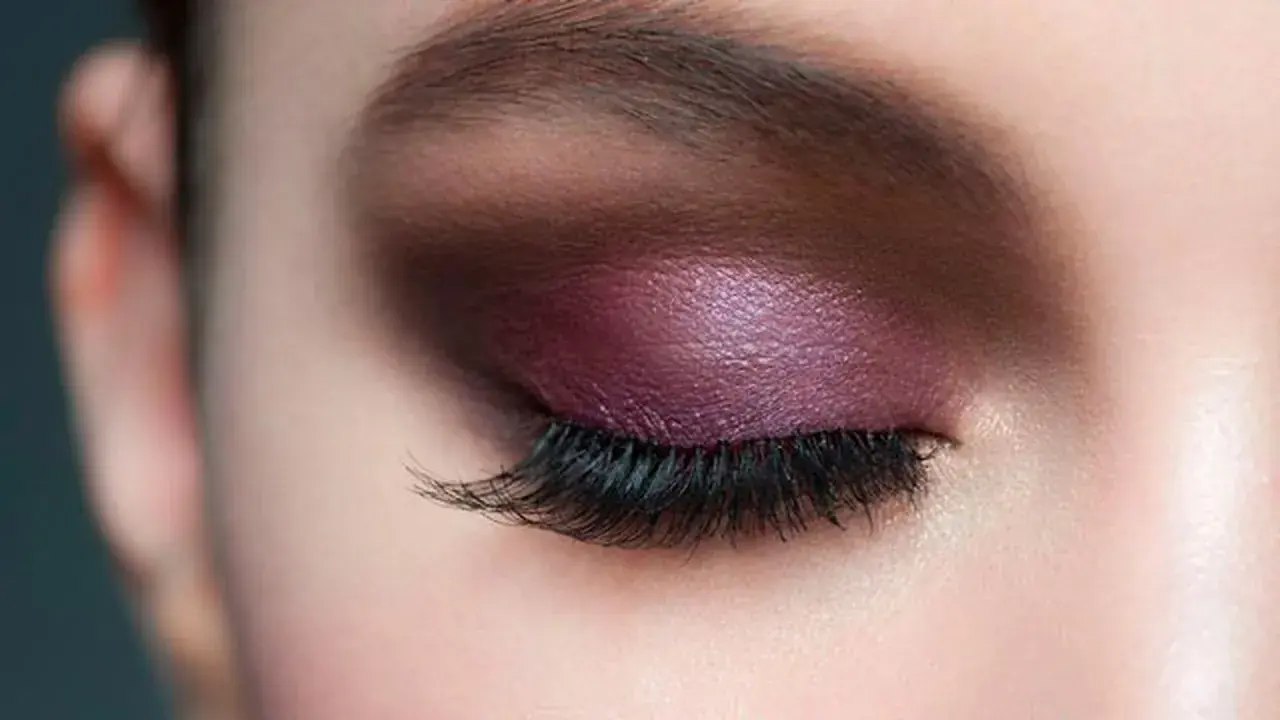Maquillaje de ojos con sombra morada brillante y pestañas largas, ideal para realzar la mirada en párpados caídos.