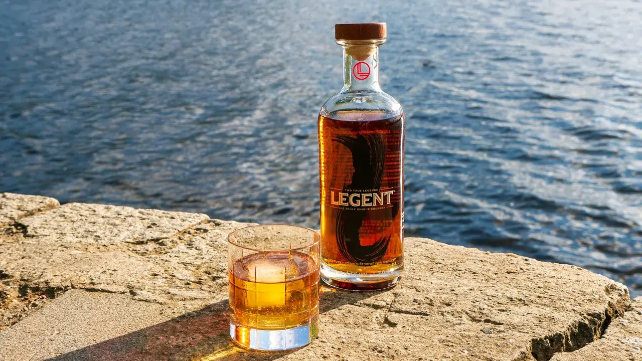 Legent Bourbon Whisky: Ein Glas und eine Flasche stehen auf einem Stein am Wasser. Was ist Bourbon Whisky? Ein Genuss für besondere Momente.