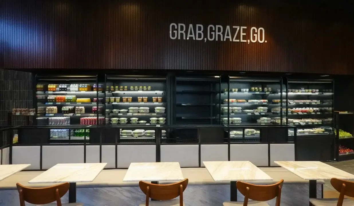 Refrigeradores llenos de comidas listas para llevar. El letrero "GRAB, GRAZE, GO" inspira una comida rápida y deliciosa.