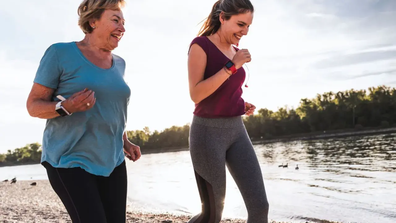 Zwei Frauen joggen am Wasser, um ihre Fettverbrennung anzuregen. Sie lächeln und genießen die Bewegung.