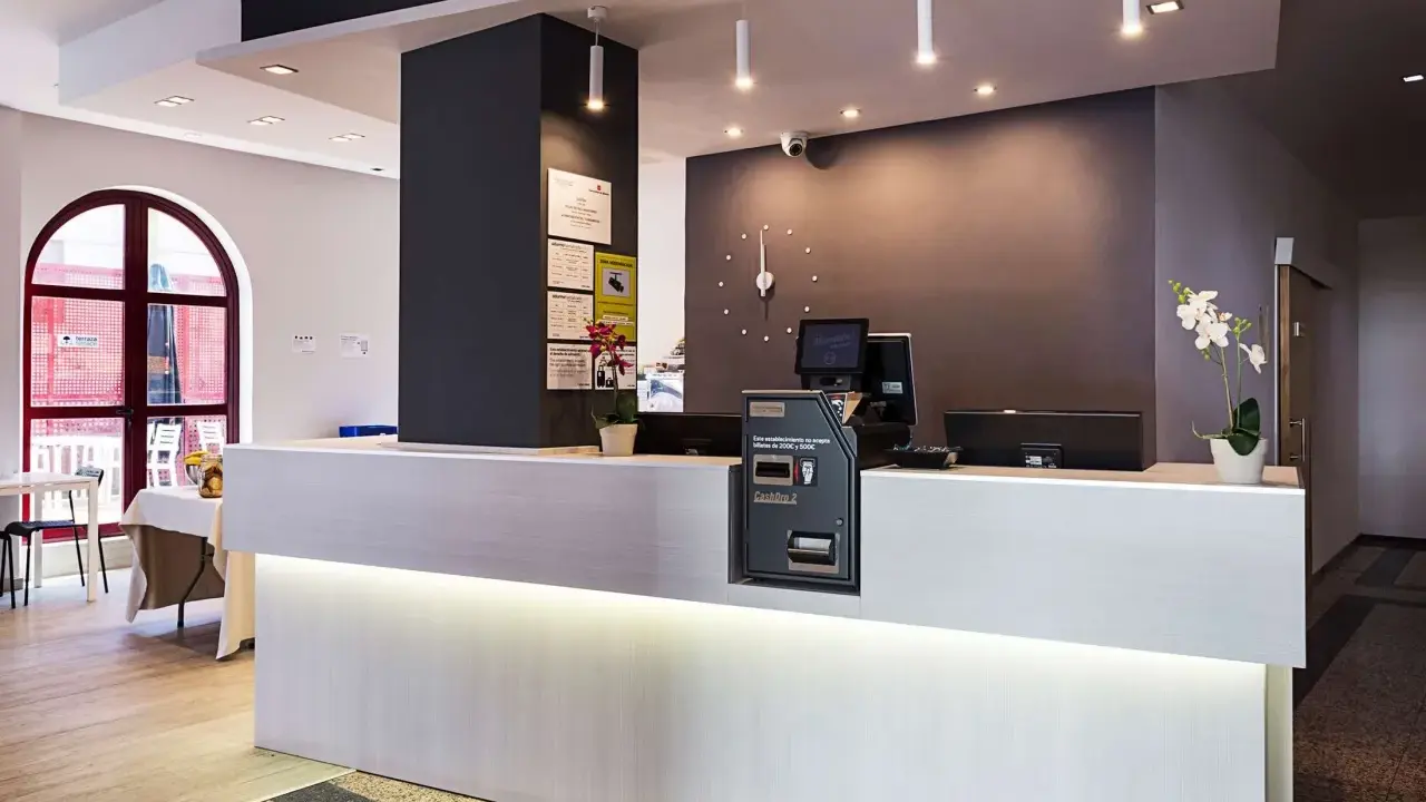 Recepción moderna y luminosa de la residencia Nuevo Versalles, con mostrador blanco, pantalla y máquina de efectivo.