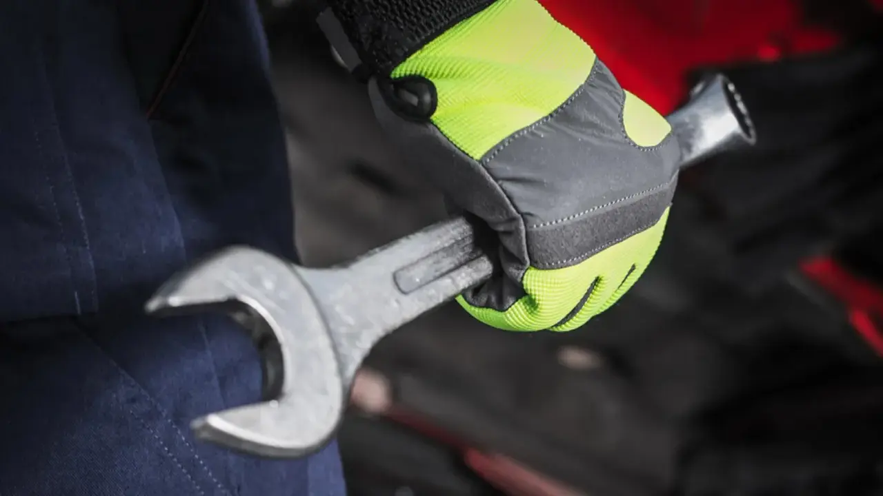 Mano con guante de alta visibilidad, parte de material de protección laboral, sujetando una llave inglesa.