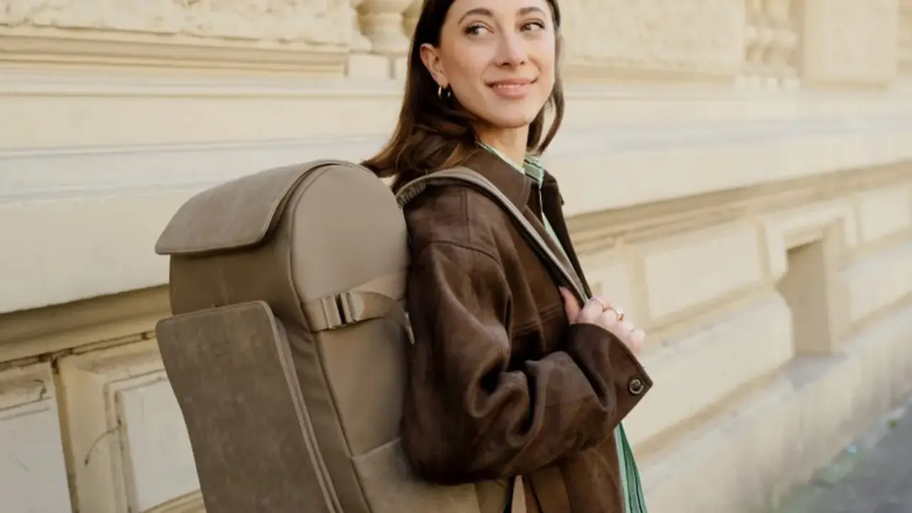 A woman smiles, showcasing the latest backpacks trend with a stylish, taupe backpack.