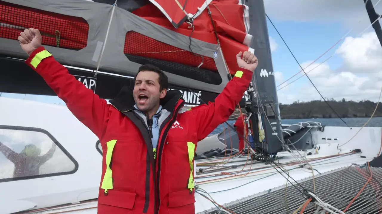 Un marinier en veste rouge célèbre sur un voilier. Une opportunité unique : ce voilier est à donner gratuitement !