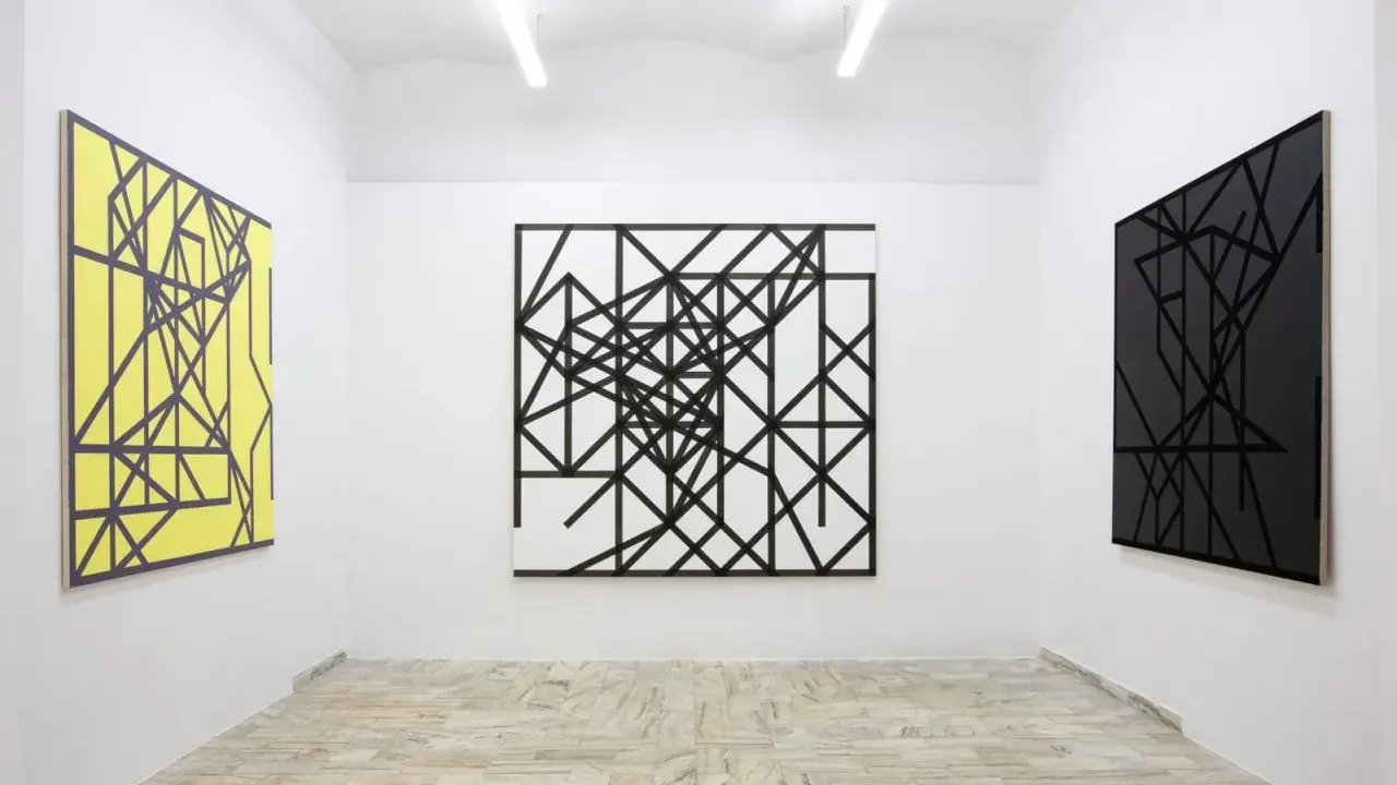 Galeria sztuki z trzema obrazami: żółtym, czarno-białym i czarnym, wszystkie w stylu abstrakcji w malarstwie, z geometrycznymi wzorami.