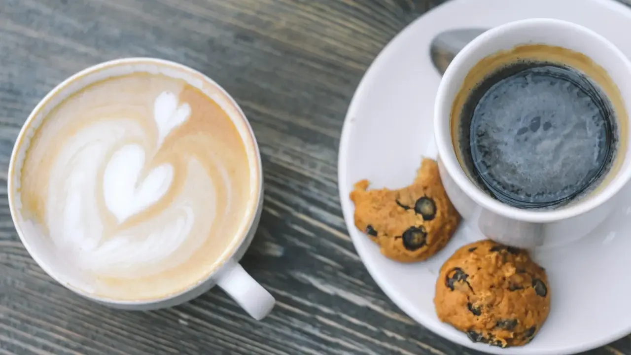 Zwei Tassen Kaffee: ein Latte mit Herz und ein starker Americano mit Keksen.