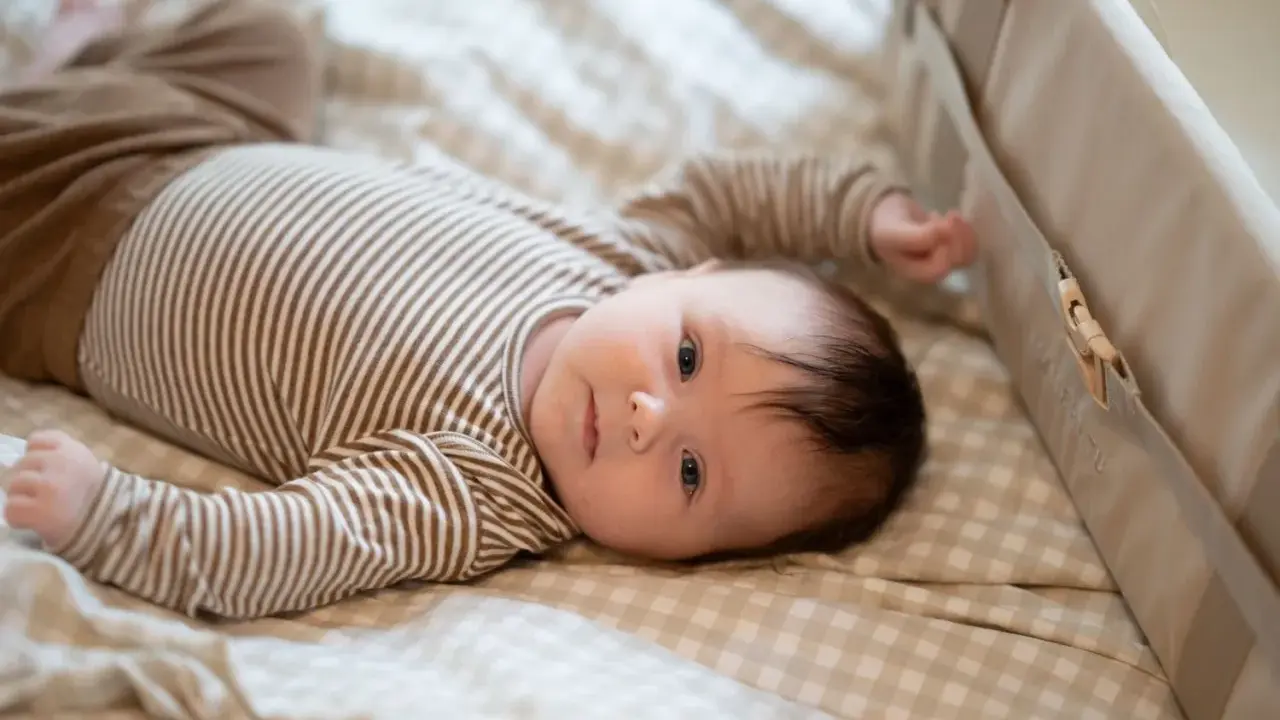 En 1 månads bebis sover inte, utan ligger vaken på en rutig filt i en säng.