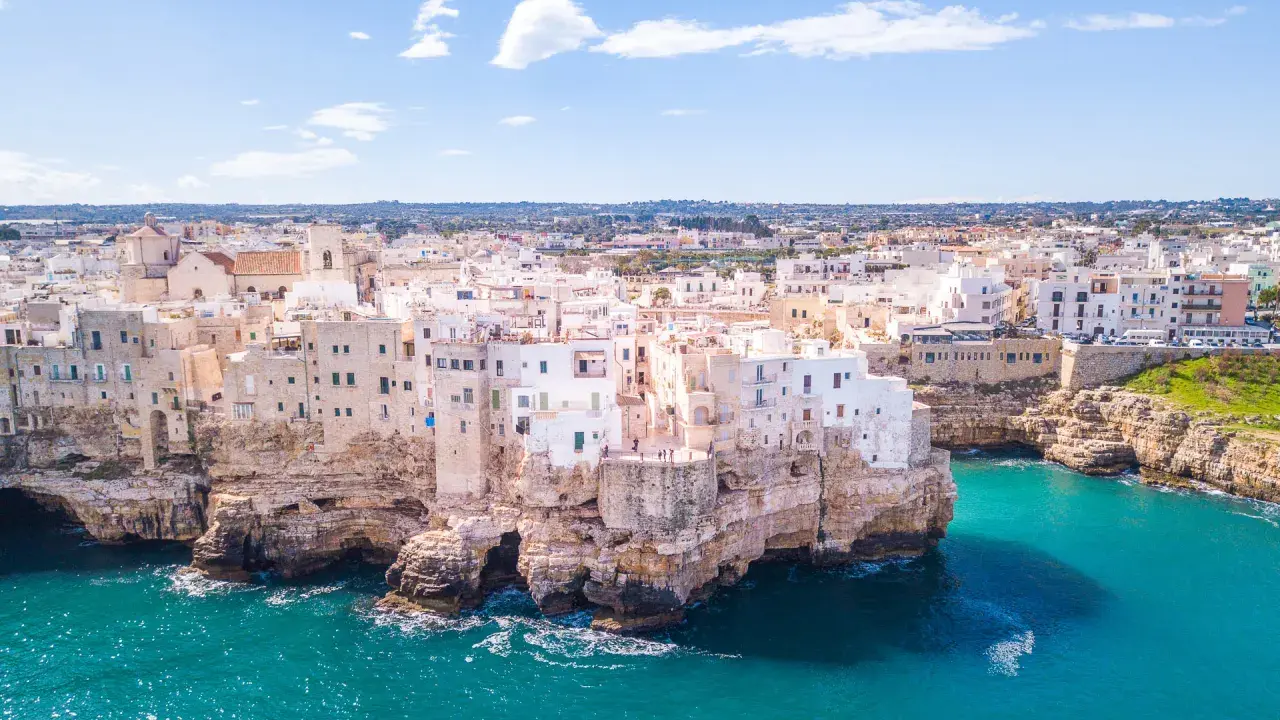 Vista aerea di Polignano a Mare, una delle più belle città da visitare in Puglia, con case bianche aggrappate alle scogliere a picco sul mare turchese.
