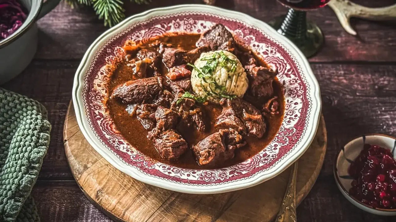 Ein festliches Hirschgulasch, wie es ein Sternekoch zubereiten würde, serviert mit Klößen und Preiselbeeren.