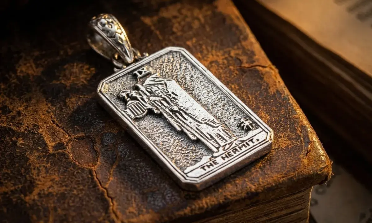 Srebrny wisiorek z motywem pustelnika tarot, leżący na starych księgach.